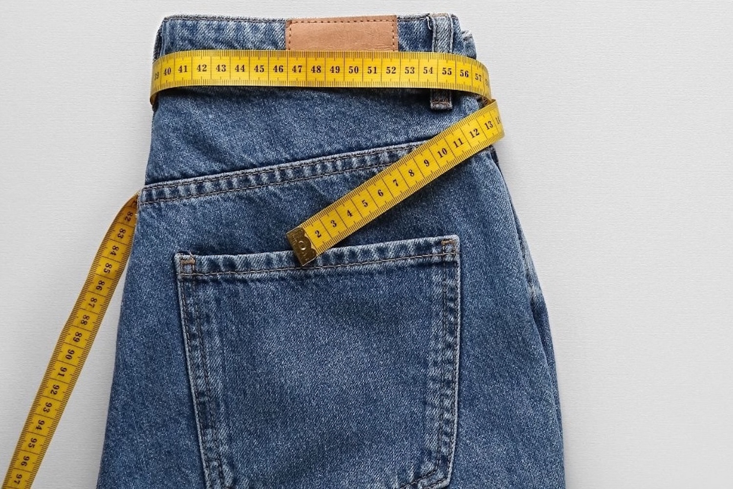 Η εικόνα ενός τζιν παντελονιού όπου στη θέση της ζώνης στην μέση είναι περιτυλιγμένη μια μεζούρα μέτρησης.